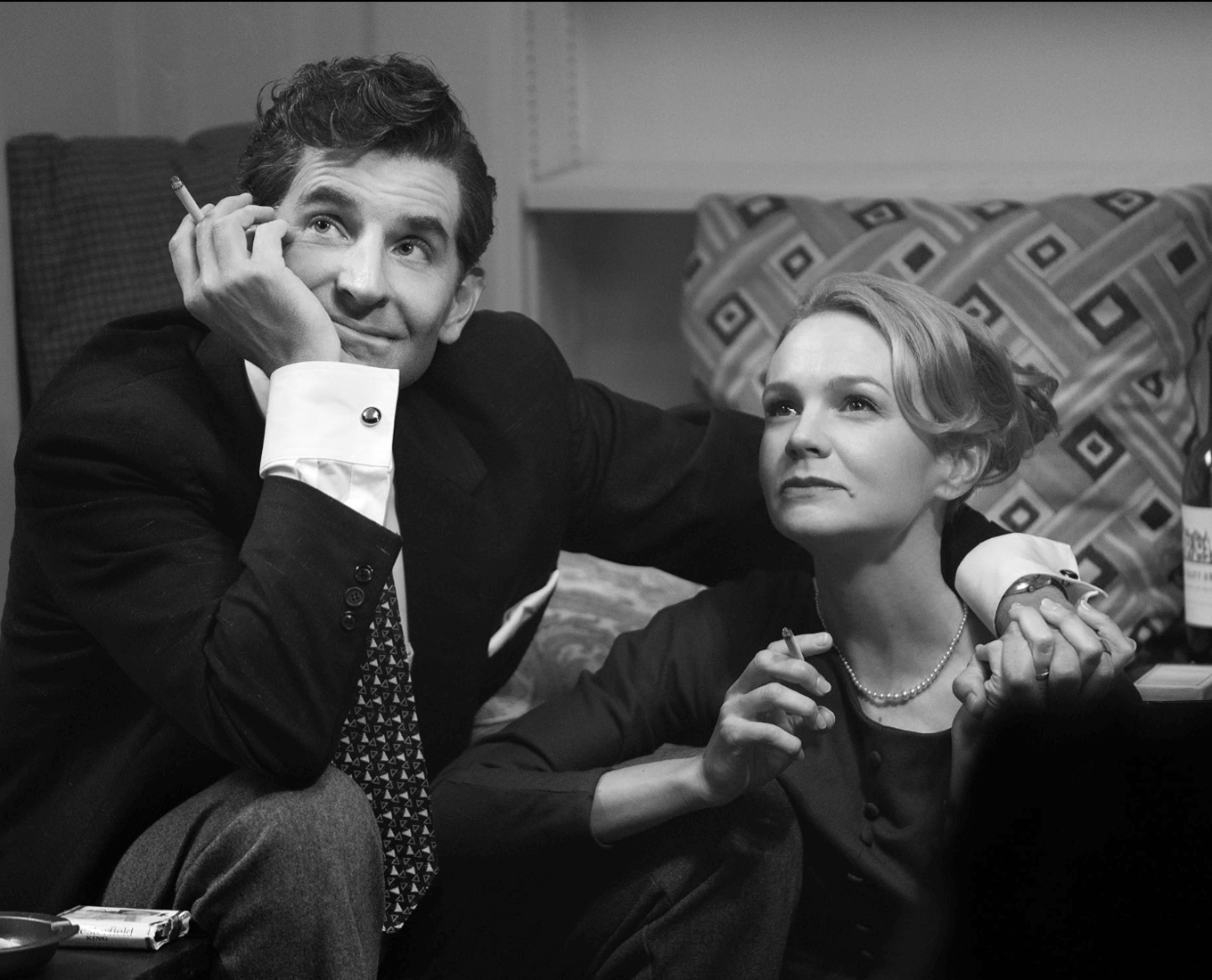 Man with a cigarette in one hand rests his arm across the shoulders of a woman