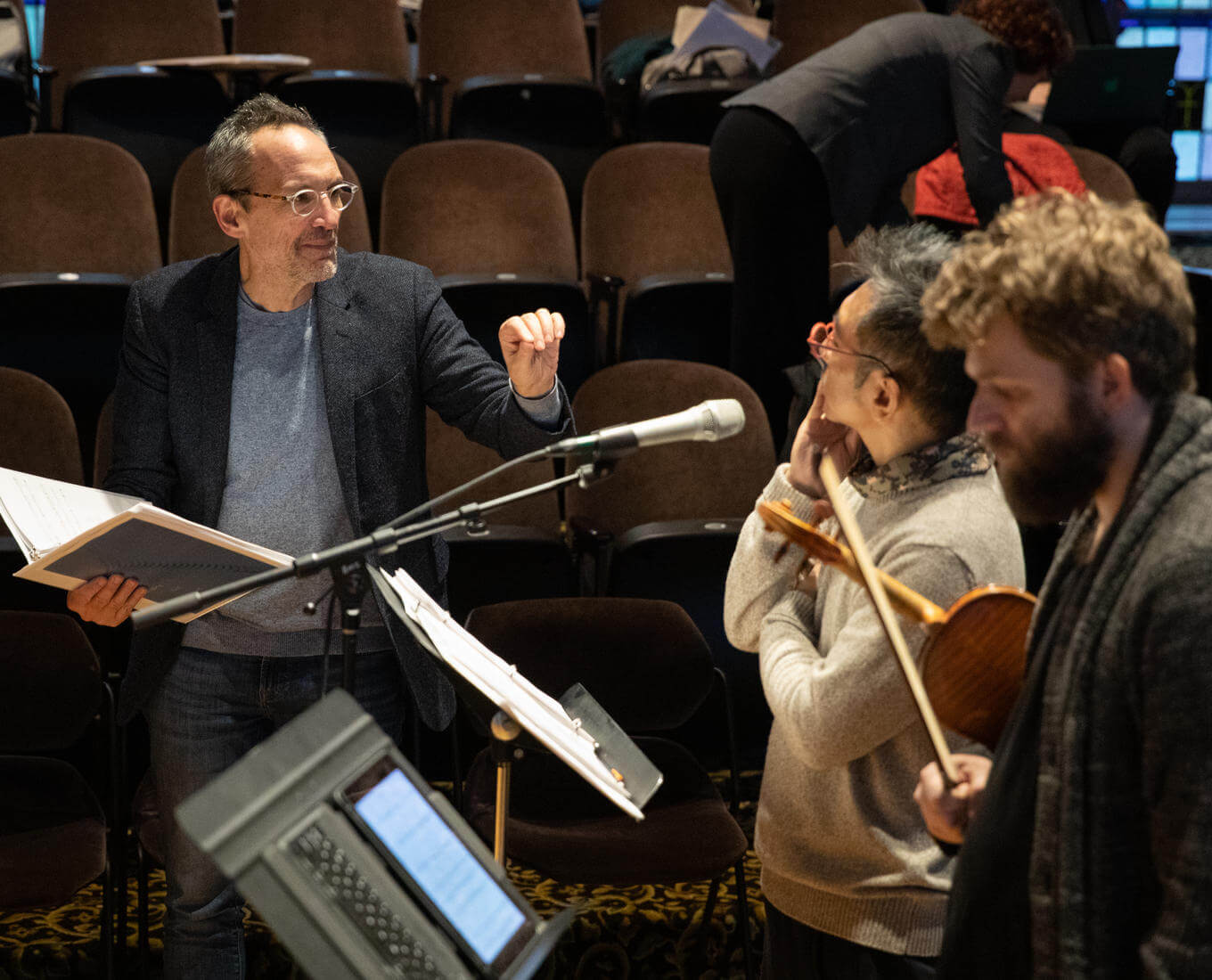 Composer talks with members of an orchestra during rehearsal.