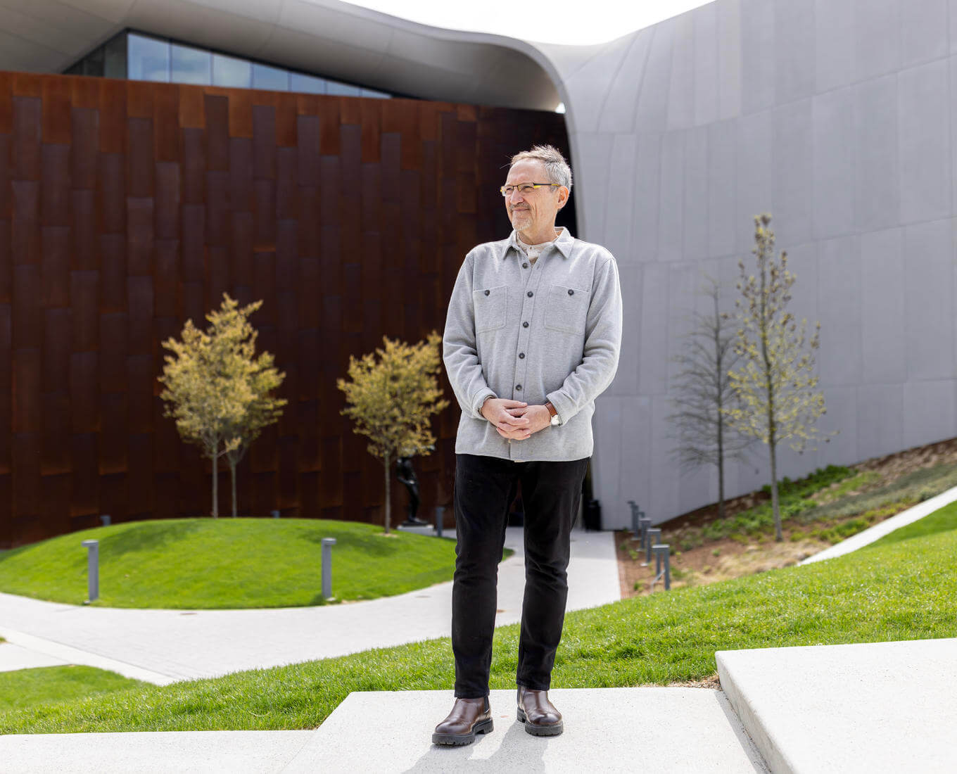 Man poses in front of building made of concrete and weathered steel walls.
