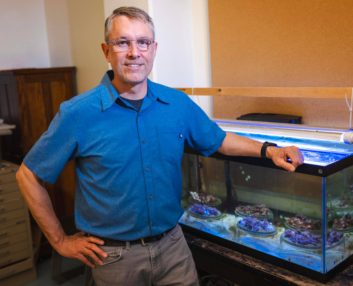 Man standing next to aquarium filled with sea coral.