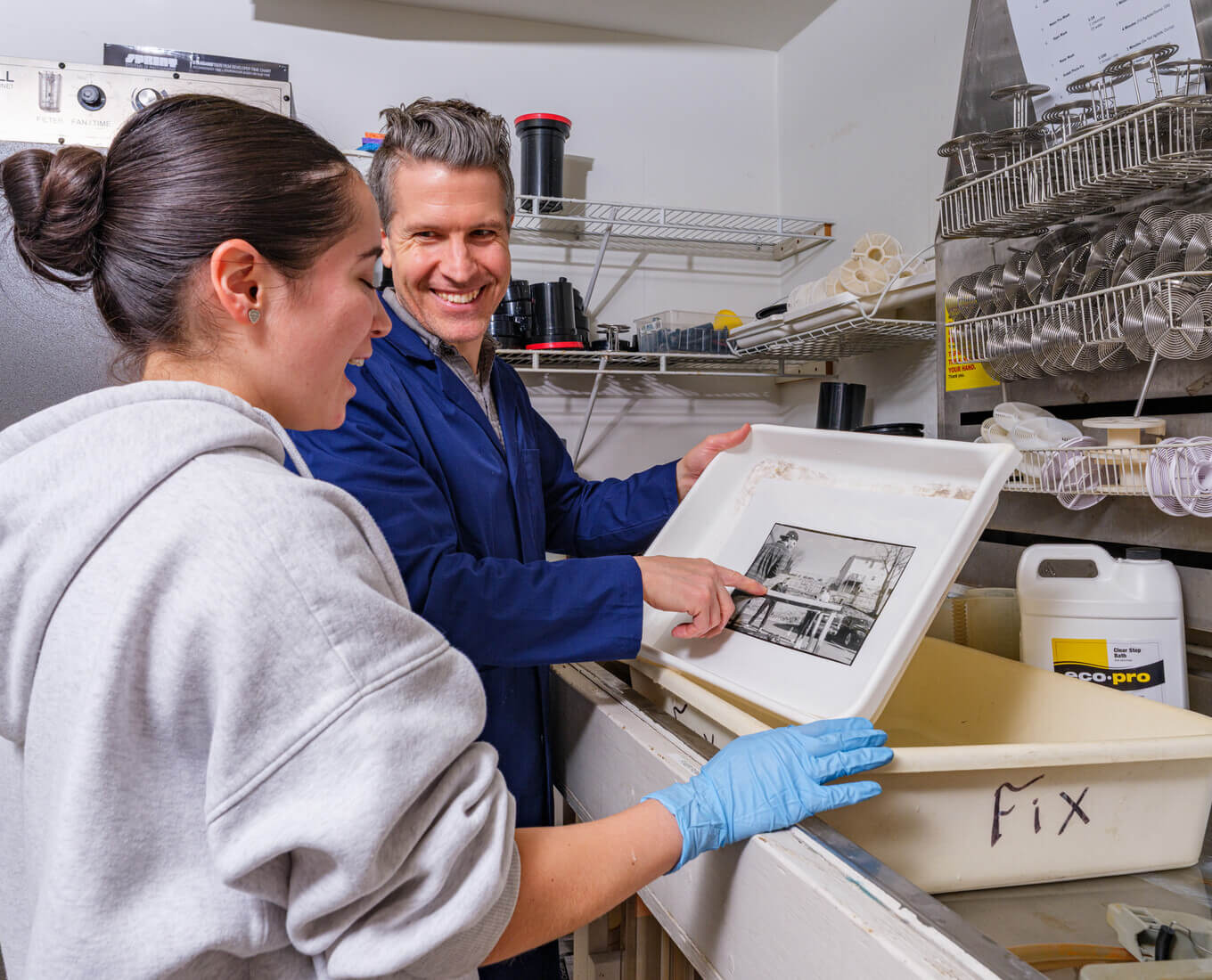 Man and woman look at print developing in a darkroom