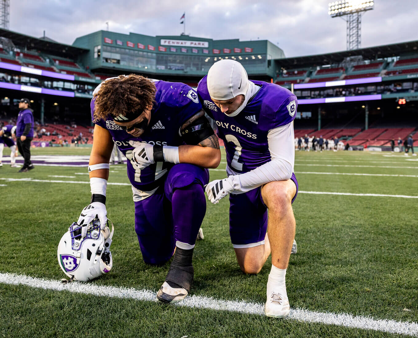 Two Holy Cross football players kneeling on the field