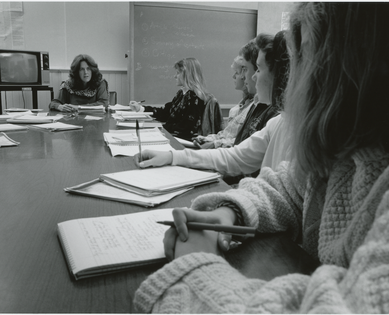 Female professor sitting at table with six female students.