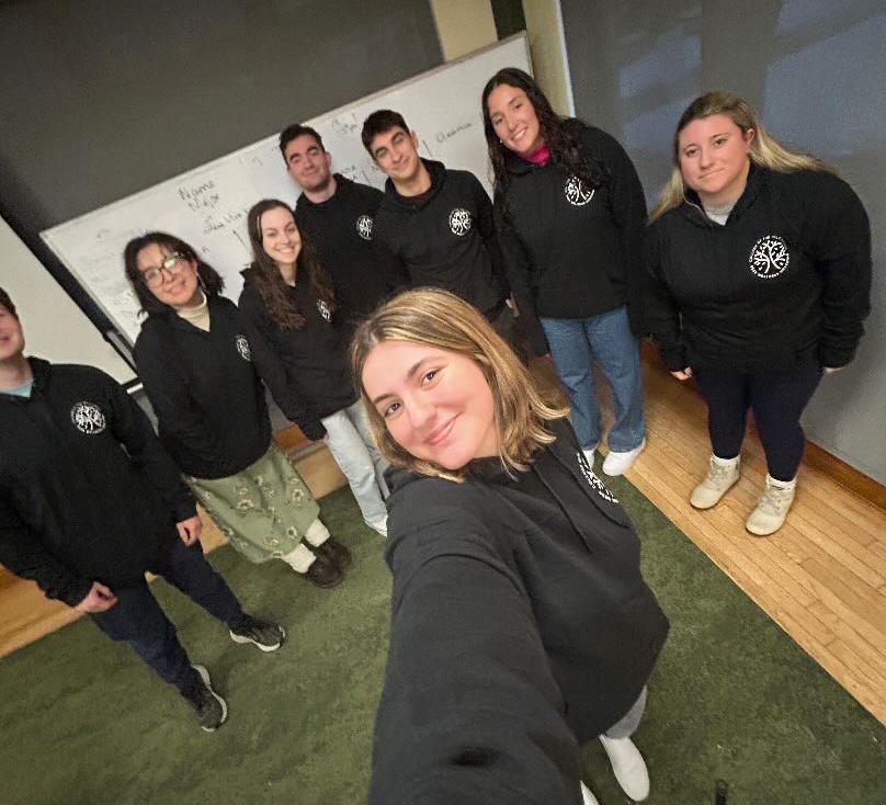 A group of students in black sweatshirts pose for a selfie.